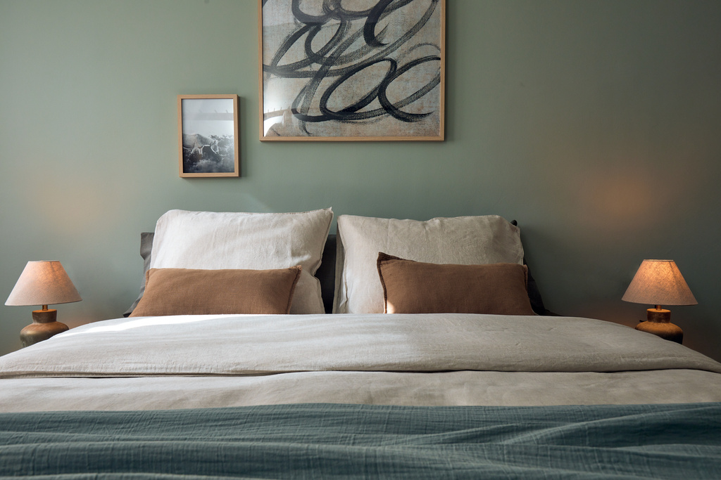 a bed in a bedroom with green walls and a painting on the wall. A neutral organic interior design, ibiza holiday home, zara home decoration, linnen sheets and art on the wall. A cozy bedroom, holiday home. Home staging, by Aptó interiors.
