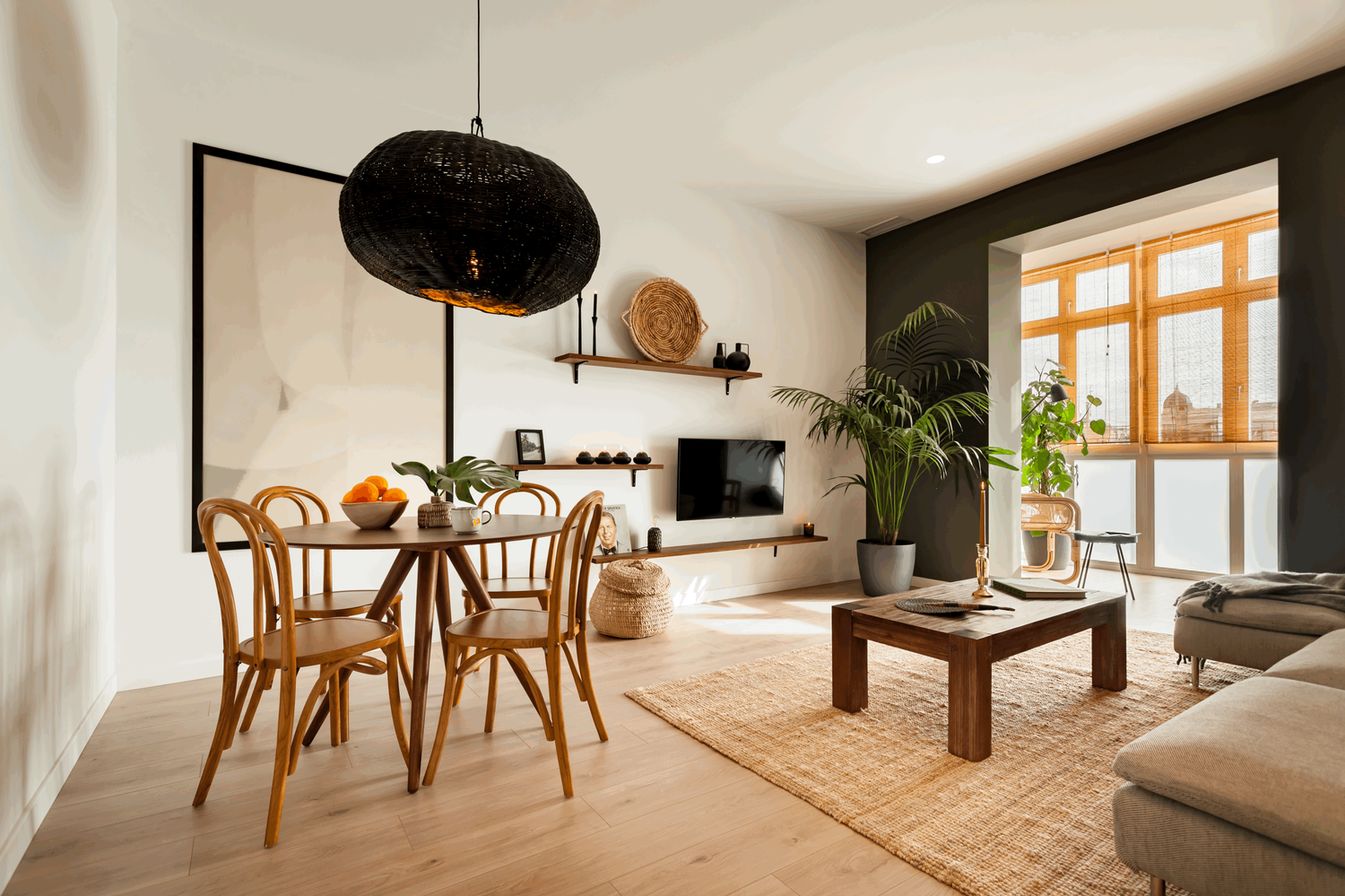a living room with a table, chairs and a tv. Elle decoration, Architectural digest, big frame on wall, wooden round dining table, big rectangle wooden coffee table, kentia palm, green painted walls, jungle home, lechuza pots, bamboo rolling curtains.