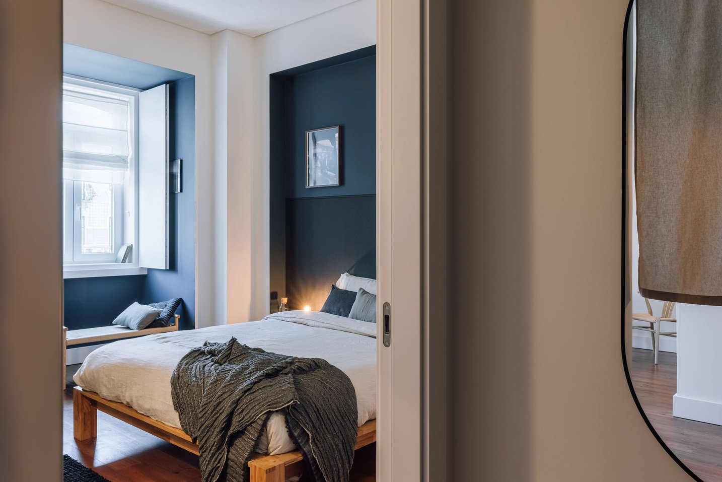 a bedroom with blue walls and wooden floors. Japanese design, linnen bed sheets, dark blue walls, wooden bedframe, minimalist and cozy bedroom design, folding curtains. Lisbon interior design. Zara home decoration. Noelle baartmans by Aptó interiors.