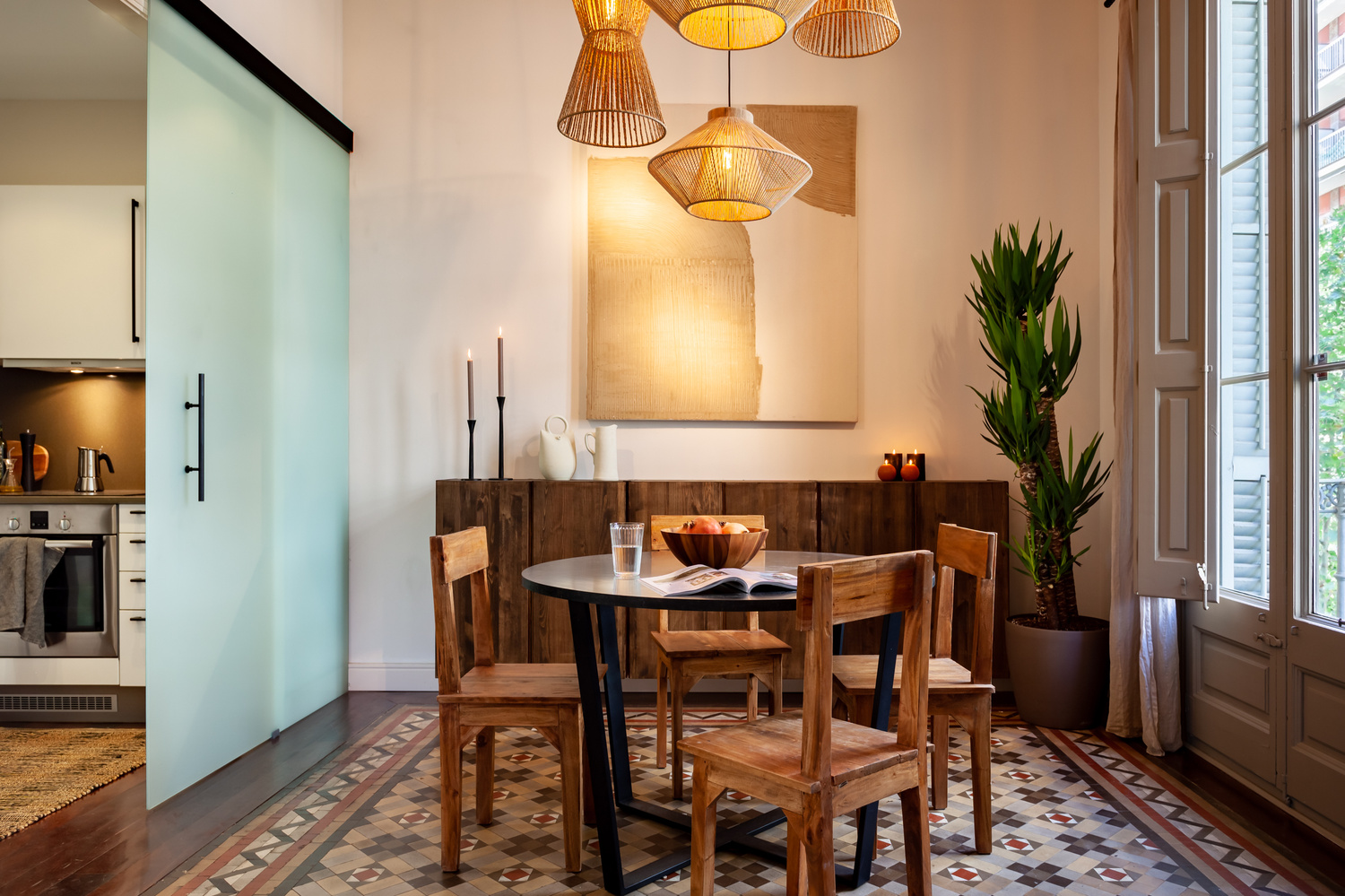 a dining room with a table and chairs in front of a window. Abstract organic wall art, ivar ikea closets, wooden dining chairs, black round wooden dining table, westwing, kave home, sklum, zara home, H&M home design, Hanging lamps, Aptó interiors