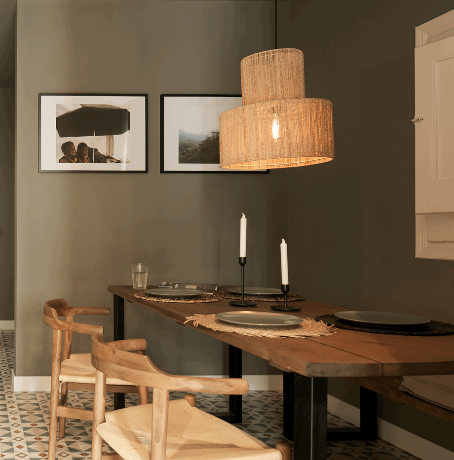 a dining room with a table and chairs. Big rectangle dining table, wooden wishbone chairs with woven seats, table setting. Wall frames decoration, woven lamp, olive green wall paint, farrow and ball by Aptó interiors Noelle Baartmans, VT Wonen